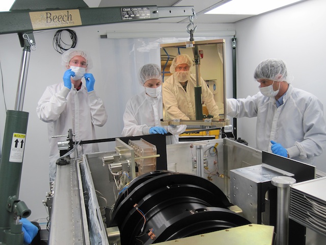APOGEE分光器の周囲で作業するSDSS-III共同研究者: 左から、Garrett Ebelke (アパッチポイント天文台)、 Gail Zasowski (オハイオ州立大)、 Steven  Majewski (バージニア大) 、John Wilson  (同)。Majewskiは部屋の反対側に立っており、設置中の反射鏡に映っている。 Image credit: Dan Long (Apache Point Observatory)